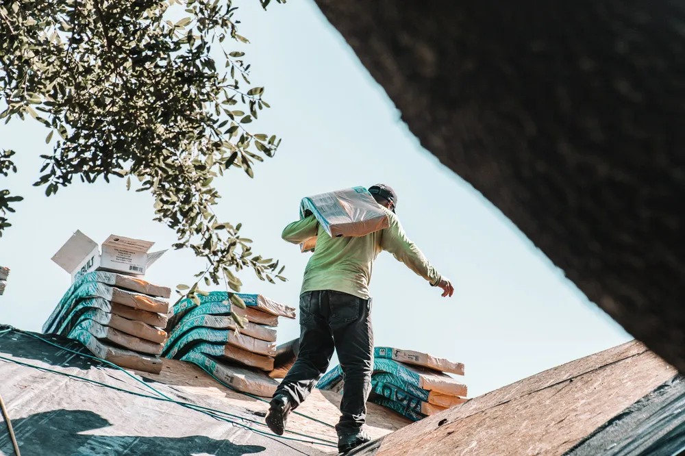 A roofer carrying shingles across a roof