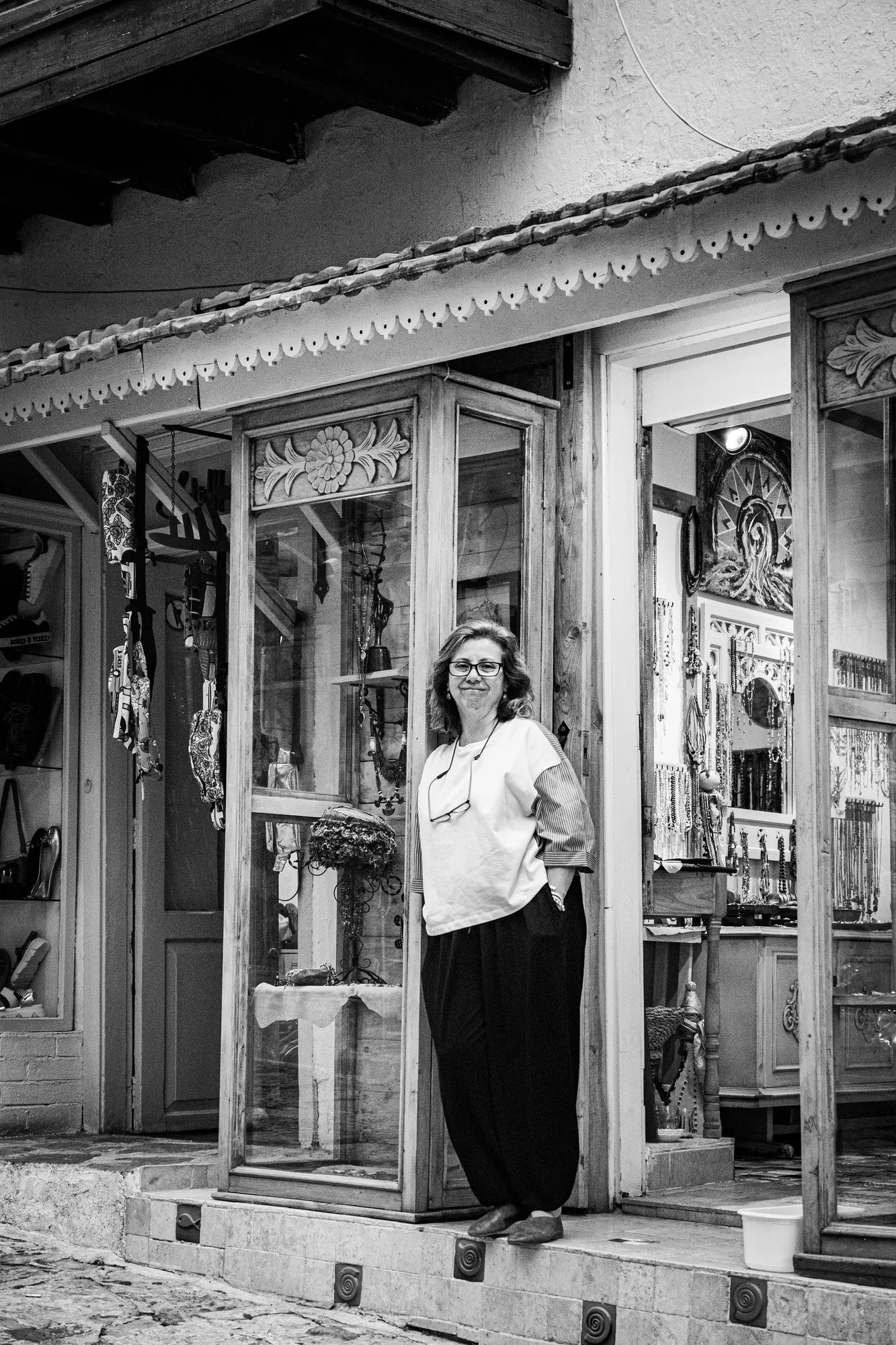 Black-and-white portrait of a shop owner standing in the doorway of her ornately carved boutique