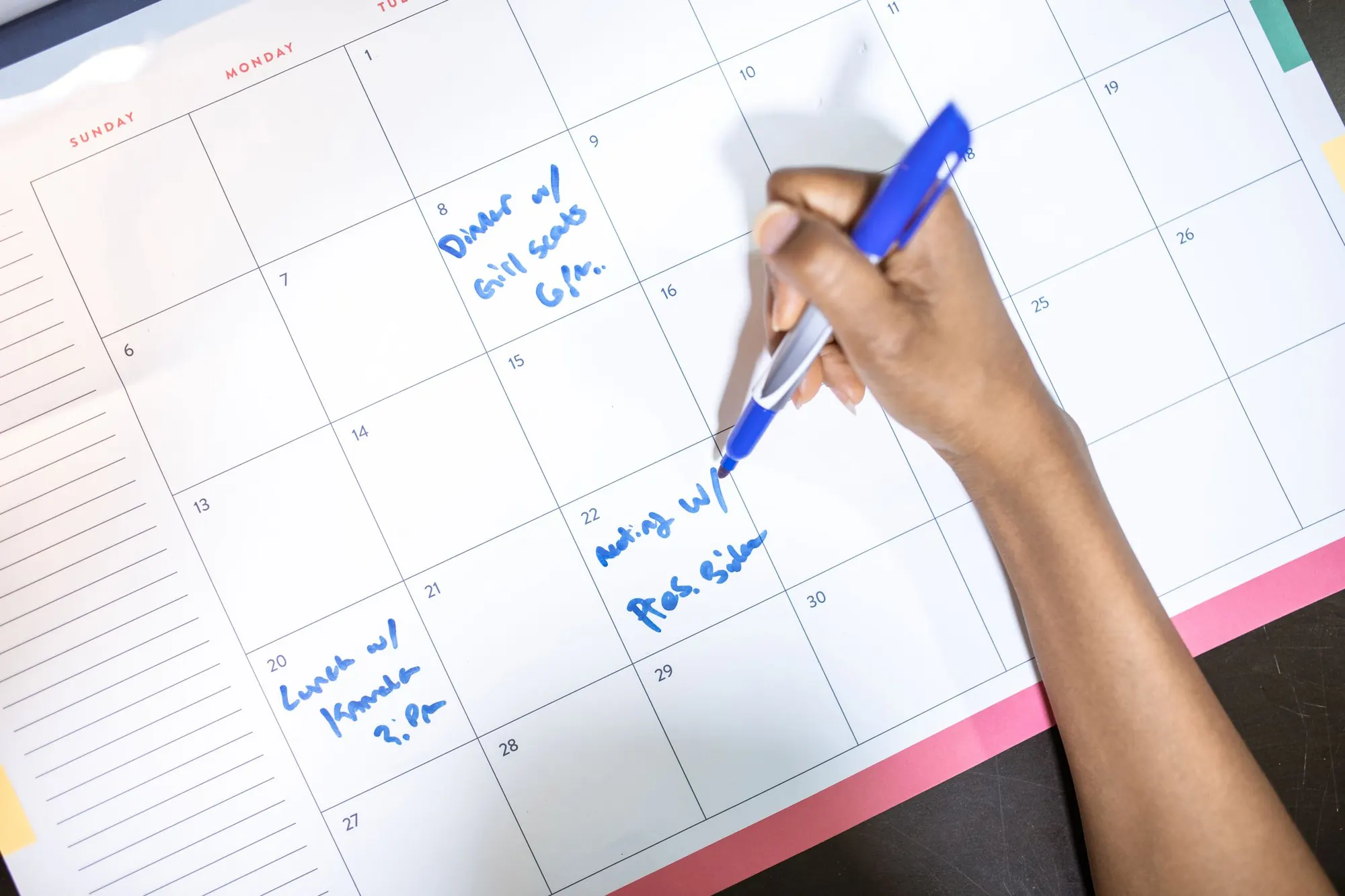A hand writing plans on a wall calendar