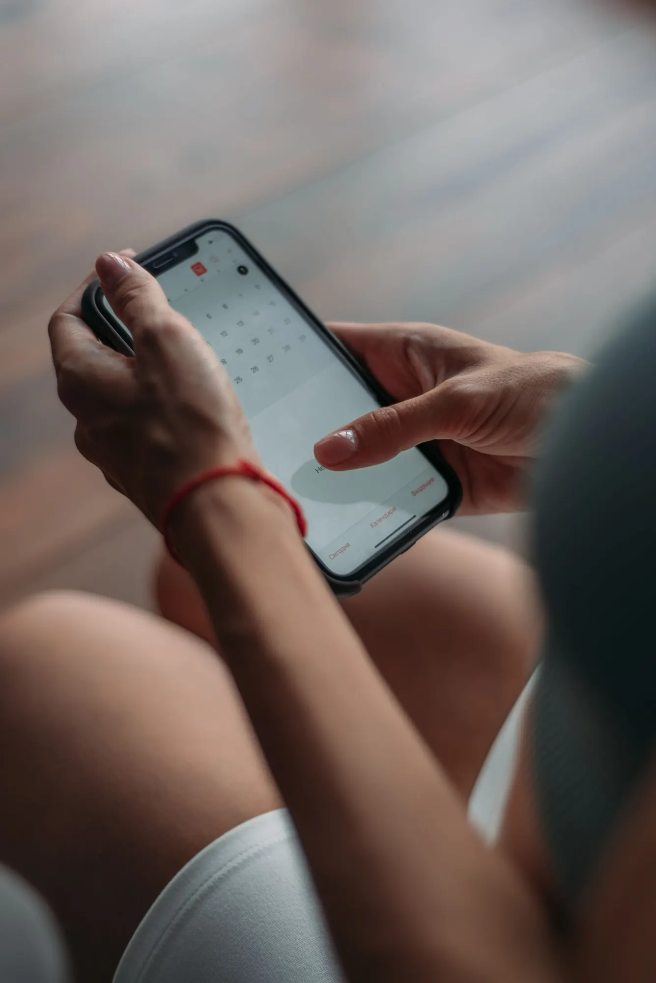 Close-up of two hands holding a phone with a calendar app open, about to tap a date