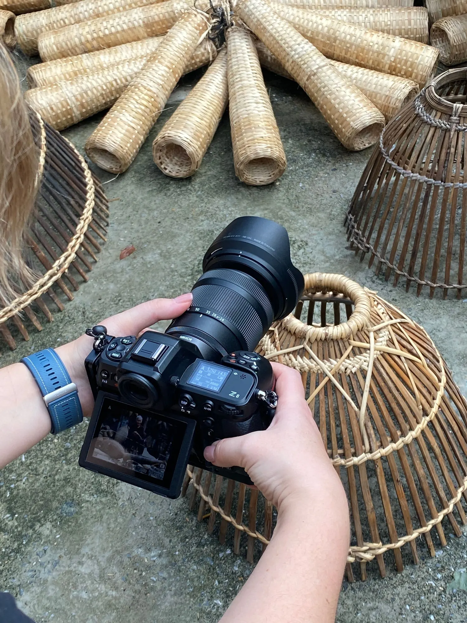 Hands hold a mirrorless camera, shooting handmade woven bamboo baskets laid out on concrete